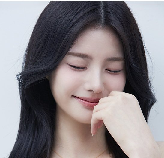 눈을 감고 미소 지으며 손끝을 코 옆에 댄 긴 머리 여성 모델